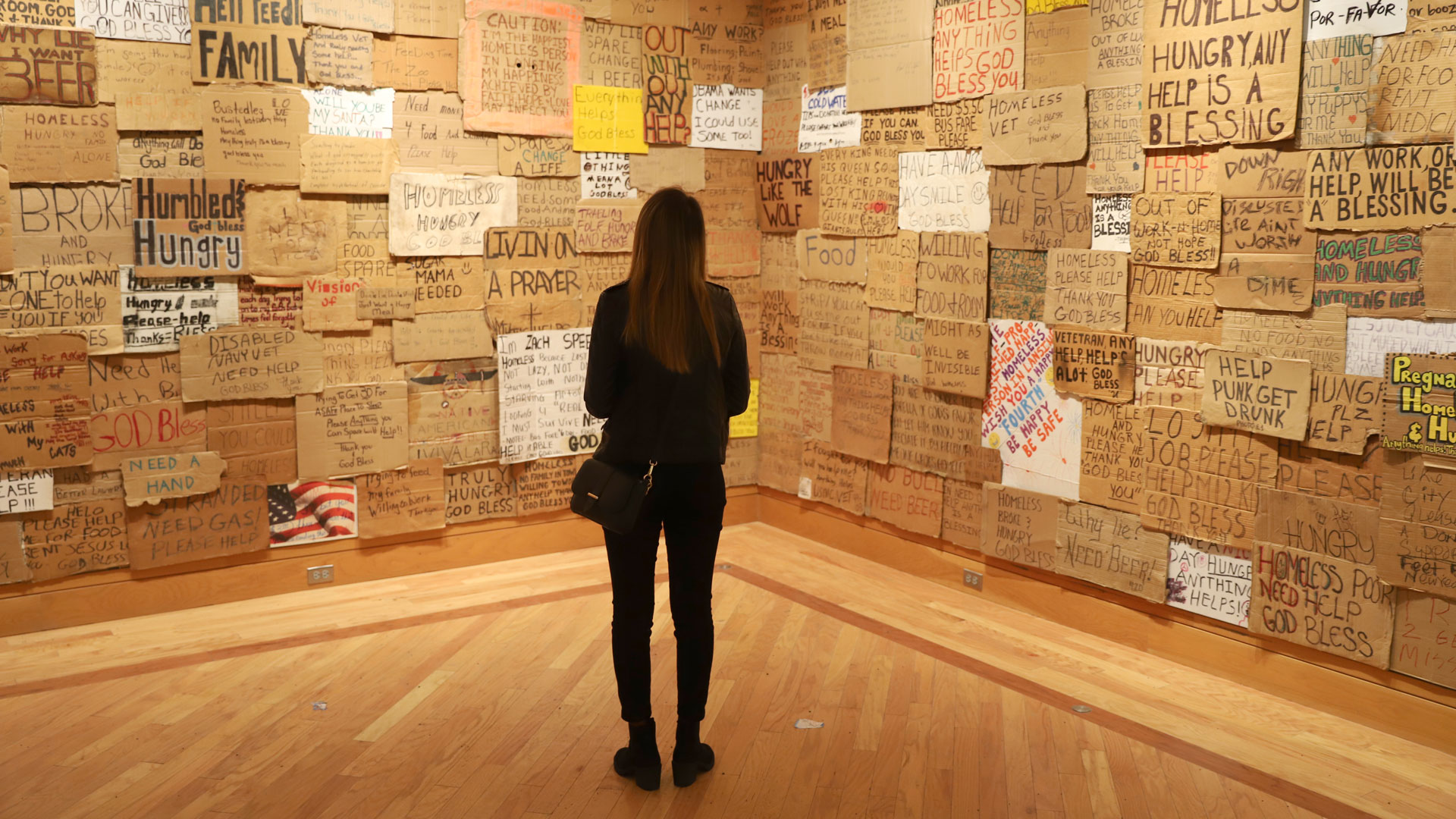 Visitor viewing a gallery wall covered floor to ceiling with handmade signs from people experiencing homelessness, Anchorage Museum 2020